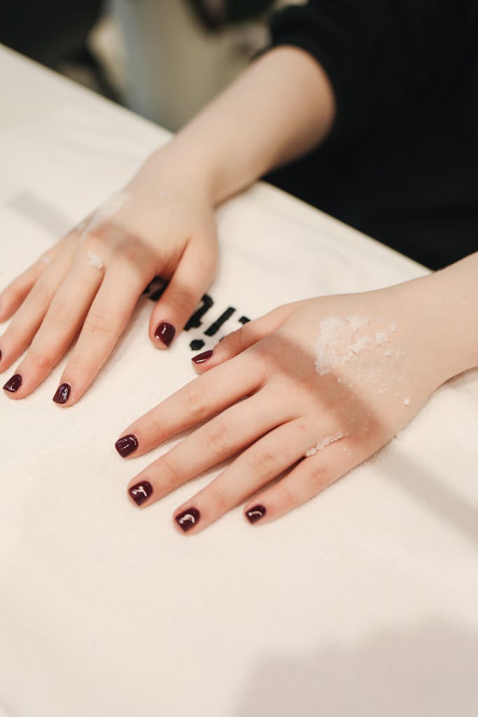 Close-up of manicured hands with burgundy nails in a beauty salon, showcasing skincare treatment.